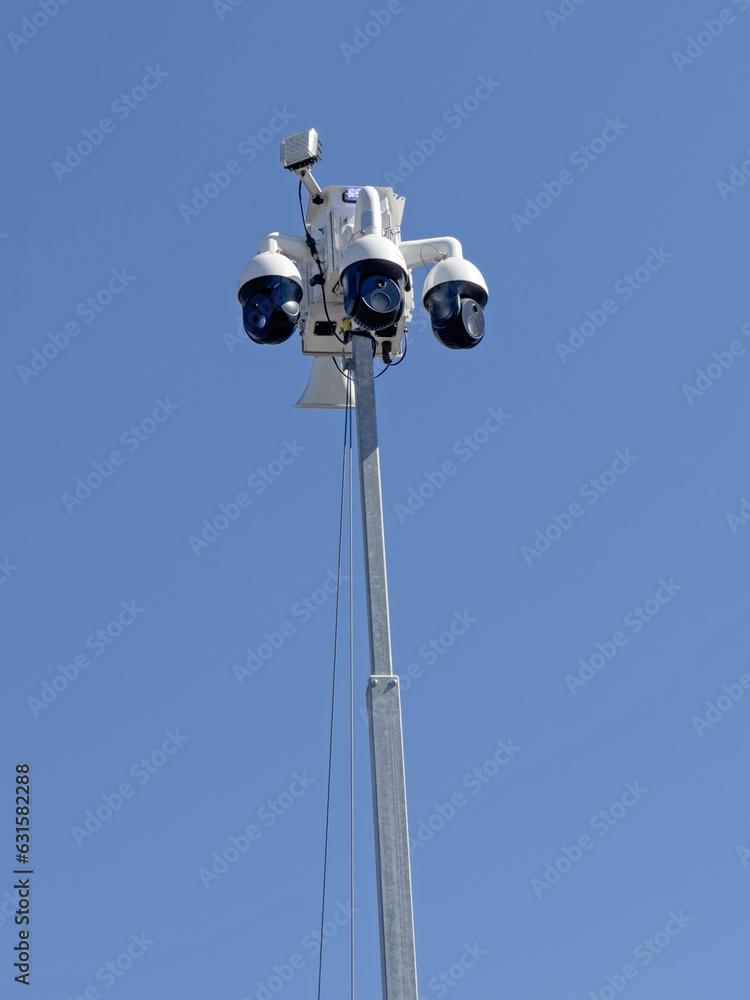 A lot cop crime prevention security camera array is shown above a retail store parking lot during the day in a vertical view. A lot cop crime prevention security camera array is shown above a retail store parking lot during the day in a vertical view.