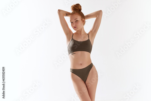 Portrait of young slim beautiful girl wearing khaki color underwear posing over white background.