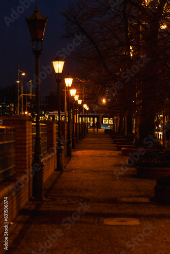 Long narrow path next to river with a lot of glowing city lamps at dark afternoon