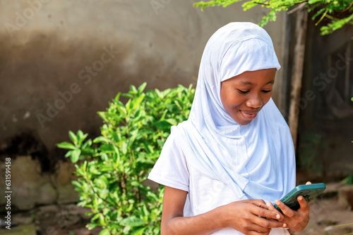 African school girl in a white hijab looking at a cell phone photo