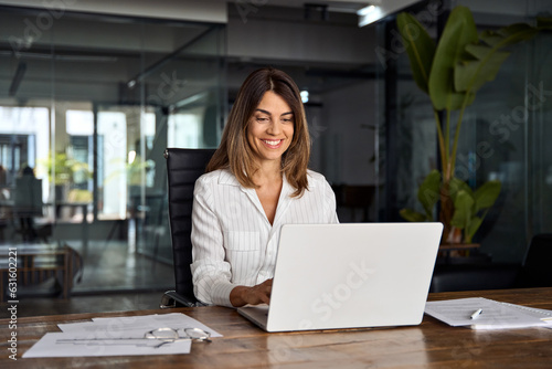 Fotografie 40s mid age European business woman CEO using laptop application for work sitting at table workspace in office