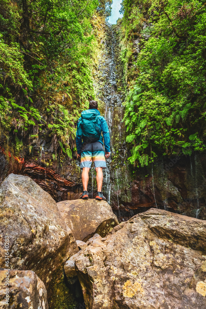 Male hiker with backpack watches green overgrown waterfall. 25 Fontes waterfalls, Madeira Island, Portugal, Europe.