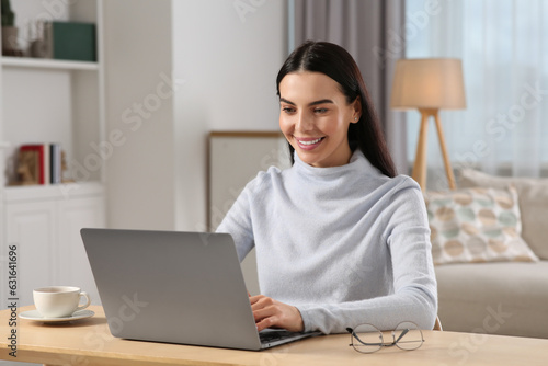 Happy woman working with laptop at wooden desk in room © New Africa