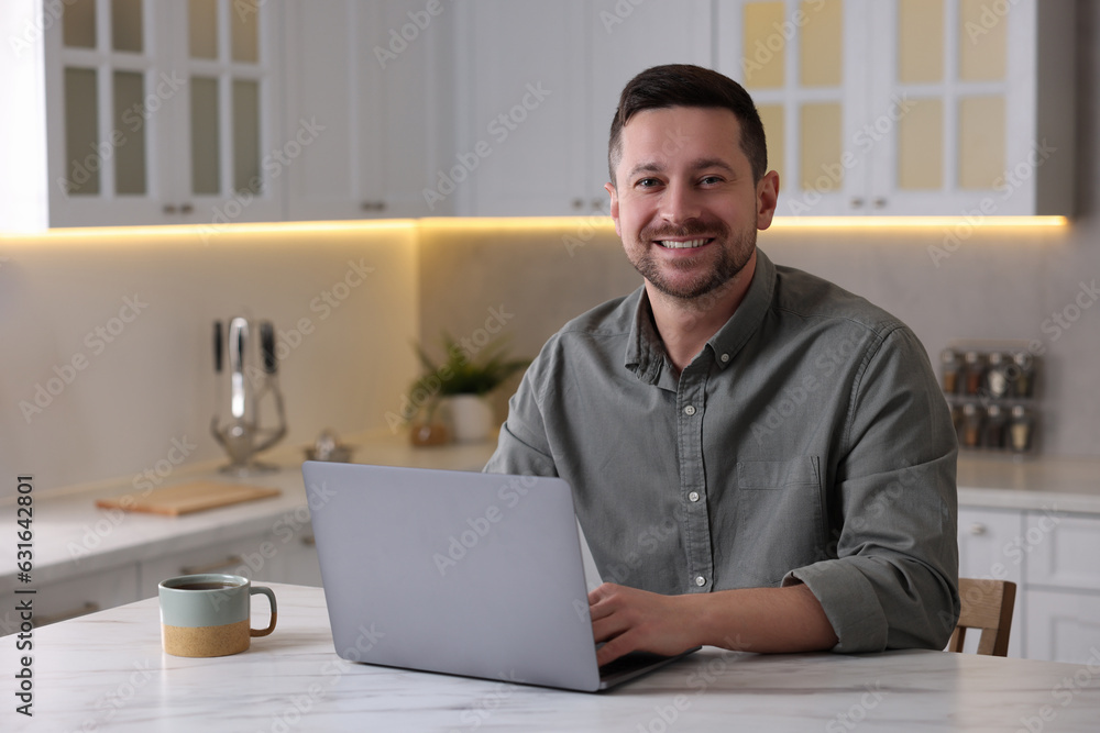 Happy man working on laptop at white marble table in kitchen