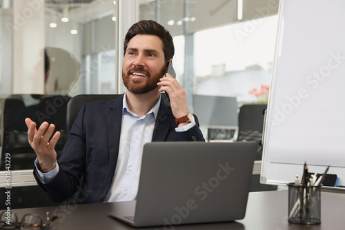 Man with laptop talking on phone at black desk in office