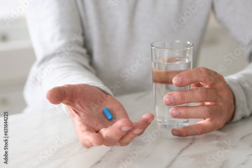 Senior man with pill and glass of water at table on blurred background, closeup