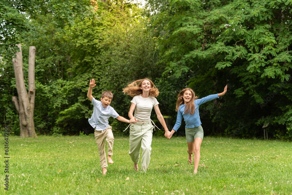 Obraz premium Three happy children running holding hands in forest outdoors. Two happy blonde teens and a little boy rejoice and run in the meadow. Happy childhood family and friendship concept. Children, lifestyle
