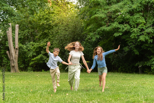 Three happy children running holding hands in forest outdoors. Two happy blonde teens and a little boy rejoice and run in the meadow. Happy childhood family and friendship concept. Children, lifestyle