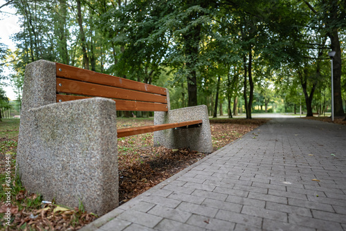 Samotna ławka stojąca w parku przy dróżce w otoczeniu zieleni podmiejskiego rejonu zachodniej Polski w porze letniej