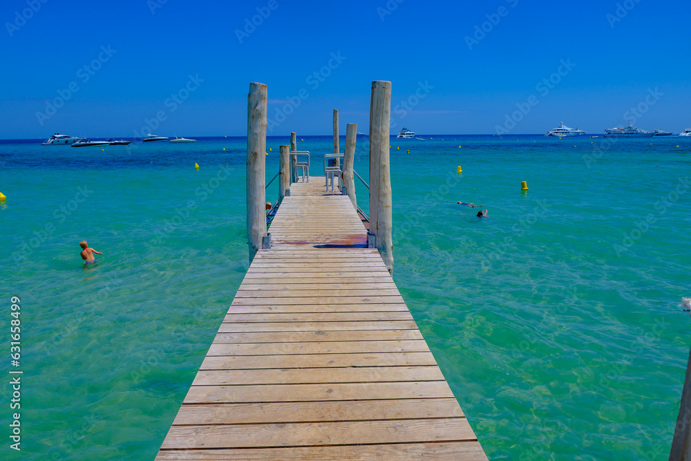 Wooden pier and crystal clear blue water of legendary Pampelonne beach near Saint-Tropez, summer vacation on French Riviera, France