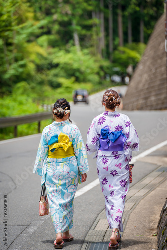 Back view of two women wearing Japanese yukata summer kimono walking on the road in nature of Kyoto, Japan. © Shawn.ccf