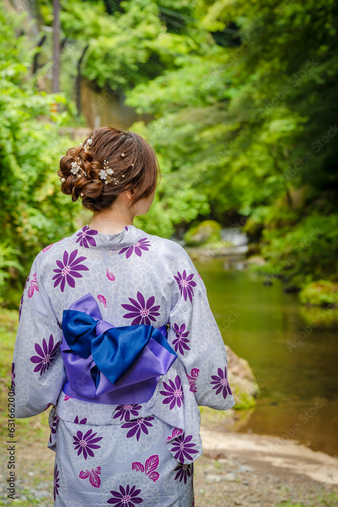 Back view of one woman wearing Japanese yukata summer kimono standing next to a river in Kyoto nature forest. Kyoto, Japan. Back view of one woman wearing Japanese yukata summer kimono standing next to a river in Kyoto nature forest. Kyoto, Japan.