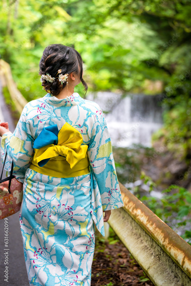 Back view of one woman wearing Japanese yukata summer kimono standing next to a river in Kyoto nature forest. Kyoto, Japan. Back view of one woman wearing Japanese yukata summer kimono standing next to a river in Kyoto nature forest. Kyoto, Japan.