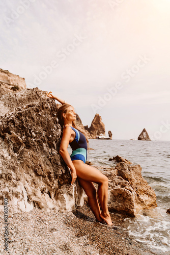 Woman travel summer sea. A happy tourist in a blue bikini enjoying the scenic view of the sea and volcanic mountains while taking pictures to capture the memories of her travel adventure.