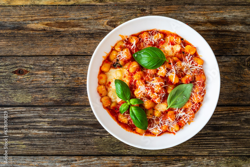 Gnocchi alla sorrentina - gnocchi with melted mozzarella cheese in tomato sauce and  Parmigiano Reggiano on wooden table
