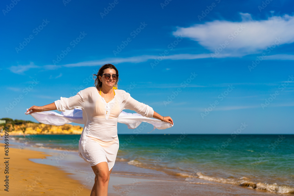 Beautiful woman walking on sunny beach holding shawl Beautiful woman walking on sunny beach holding shawl