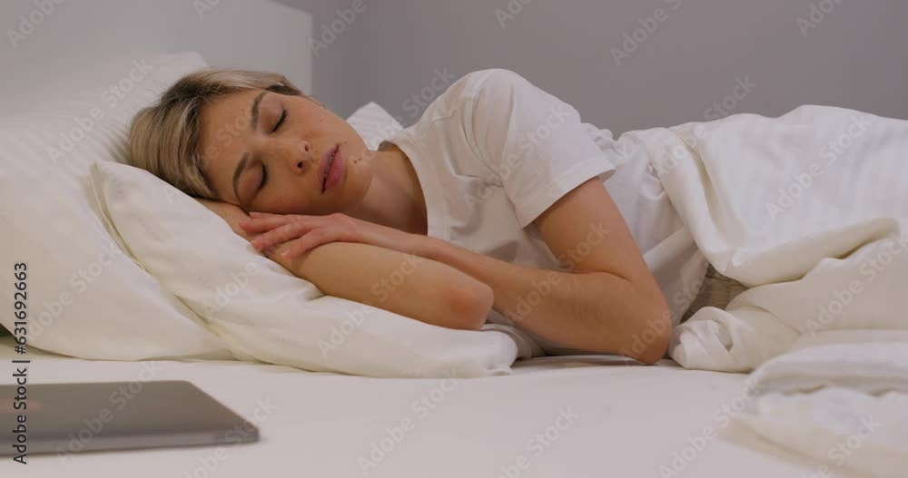 young lonely fair-haired woman stroking her arm, sleeping on cosy bed, relaxed blonde girl has rest on bed in the bedroom Slow motion tiredness Relaxation Time to sleep, laptop in the foreground young lonely fair-haired woman stroking her arm, sleeping on cosy bed, relaxed blonde girl has rest on bed in the bedroom Slow motion tiredness Relaxation Time to sleep, laptop in the foreground