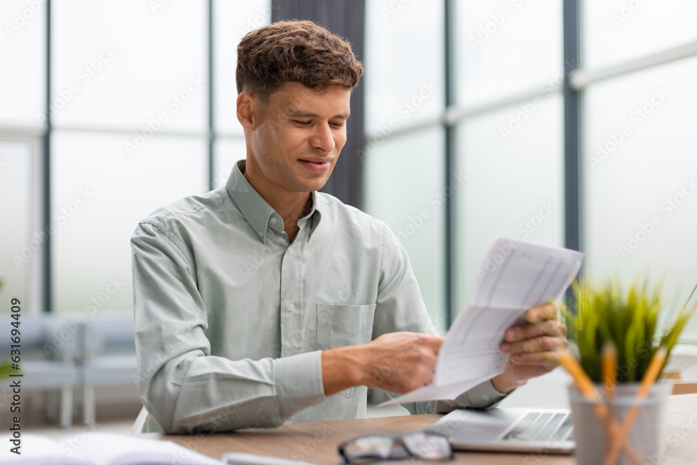 Young man is working with papers while sitting in the office. Successful entrepreneur is studying documents with attentive and concentrated look. Young man is working with papers while sitting in the office. Successful entrepreneur is studying documents with attentive and concentrated look.
