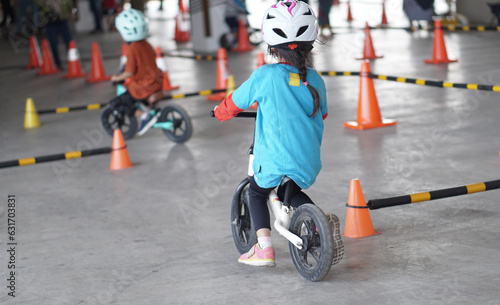 young girls 5 years old races on balance bike in a parking area with cones as track, back view, behind view shoot.