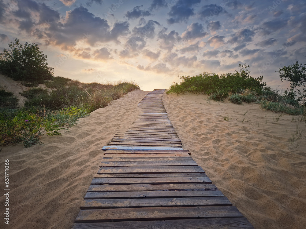 Fototapeta premium Wooden path through the sand leading to the beach. Beautiful morning sky with fluffy clouds