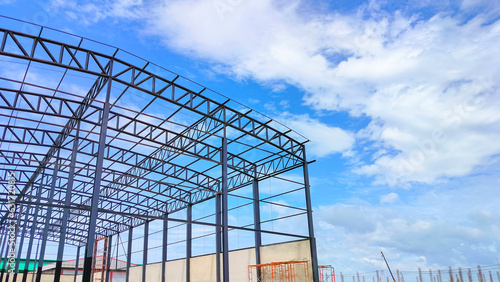 Metal roof beam and columns of warehouse building structure in construction site area against clouds on blue sky background, Low angle and perspective side view