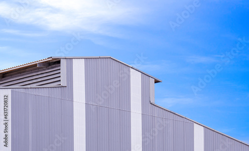 Gray and white corrugated metal wall with louver and rooftop of modern industrial building against blue sky background  perspective side view