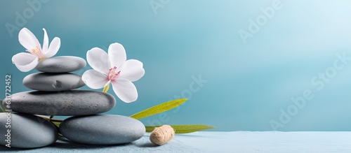 A tranquil spa and wellness concept with a pile of Zen stones, flowers, and towels placed on a light blue background with room for text. A calm and soothing treatment that promotes relaxation. A