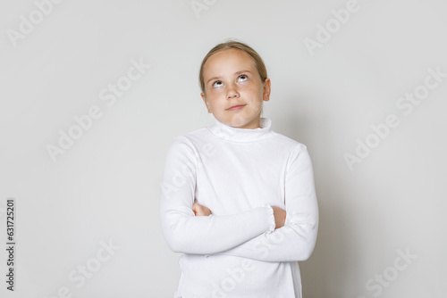 Child with crossed arms looking up on whitestudio wall background. Young girl 10 years old, studio portrait