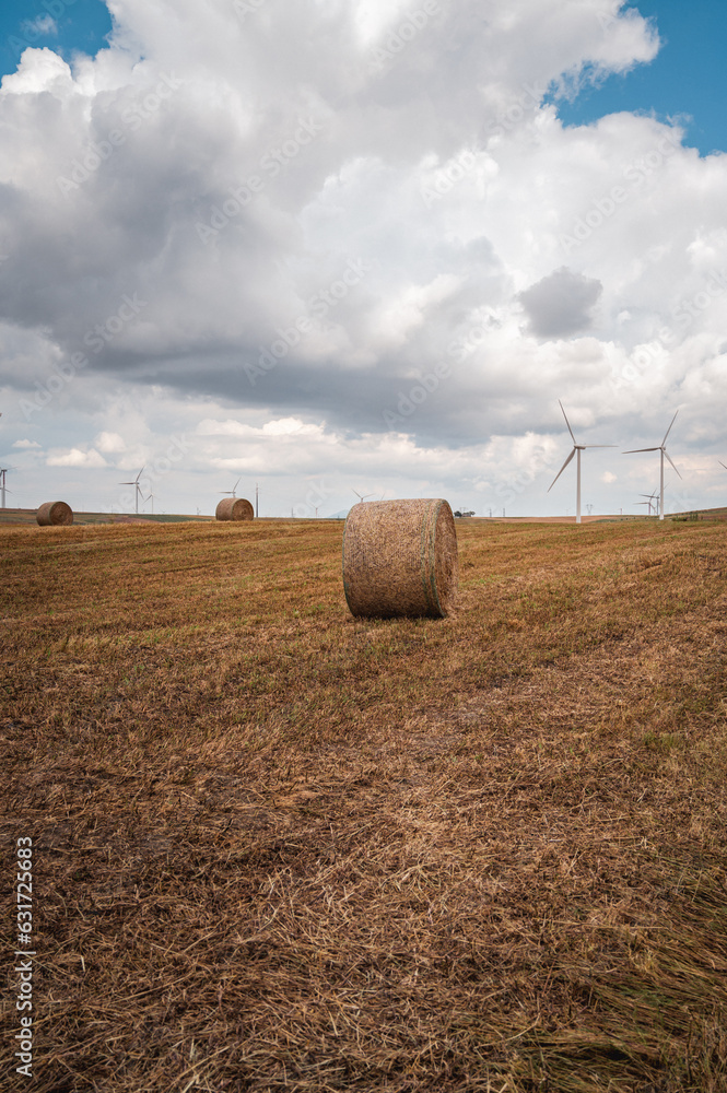 wind farm with freshly harvested wheat field with straw bales. In the distance an ominous stormy sky with black clouds