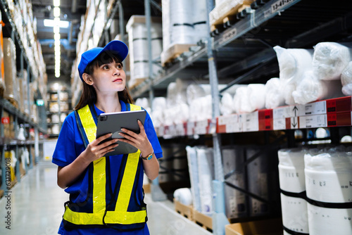 Female worker uses a digital tablet computer to check inventory in a warehouse full of goods. Distribution center concept.
