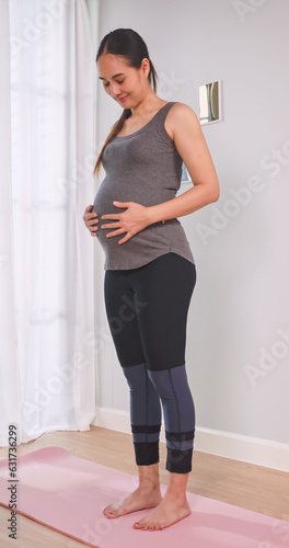Asian pregnant woman in sportswear doing exercise in living room at home.