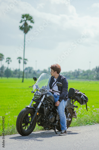 asian young man is sitting on cruiser motorcycle with green fiel