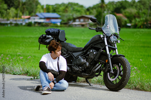 Fototapeta asian young man is sitting on road with cruiser motorcycle and g
