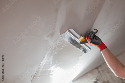 The master hand with a wide spatula applies white putty to the wall - leveling the wall into a plane for painting and wallpaper photo