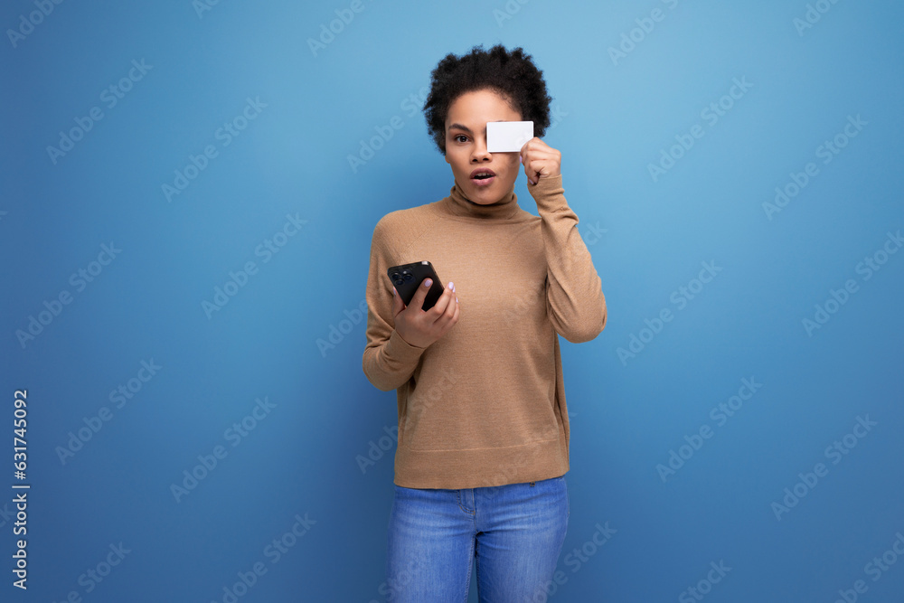 Fototapeta premium isolated with background, well groomed pretty young brunette hispanic woman with ponytail hairstyle holding credit card and phone