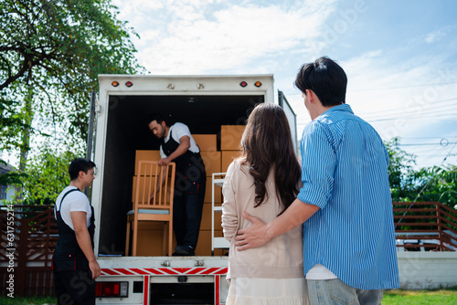Asian Couple check while unloading boxes and furniture from a pickup truck to a new house with service cargo two men movers worker in uniform lifting boxes. concept of Home moving and delivery. photo
