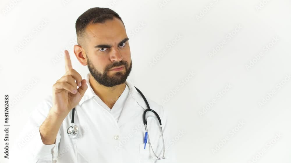 Young male doctor pointing right and saying no with his finger. Looking at camera isolated on white background Young male doctor pointing right and saying no with his finger. Looking at camera isolated on white background