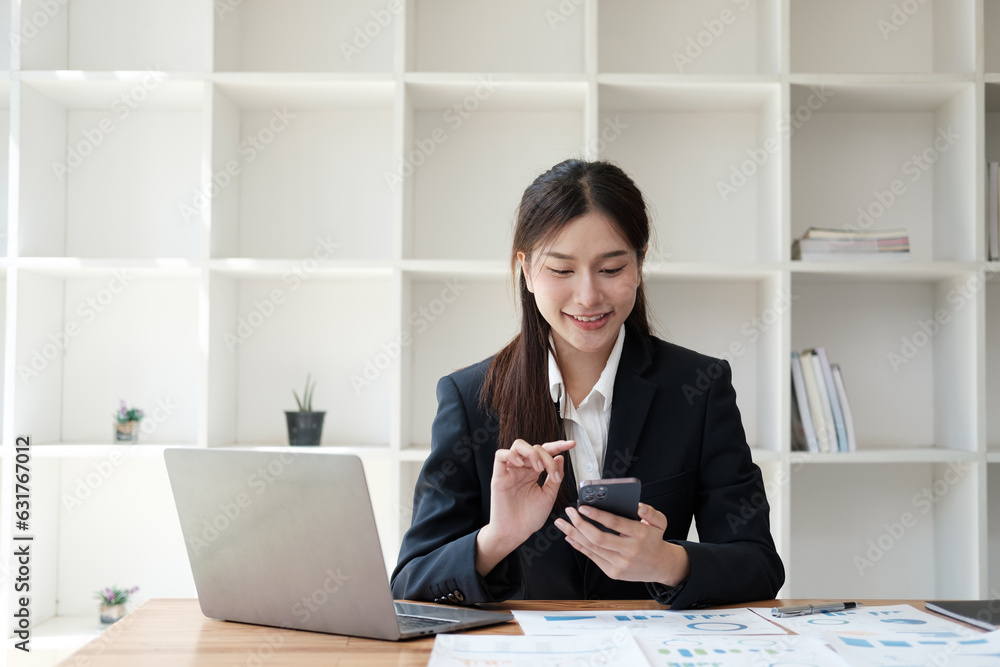 Young beautiful Asian businesswoman working with laptop computer while using smartphone in her office room. Young beautiful Asian businesswoman working with laptop computer while using smartphone in her office room.