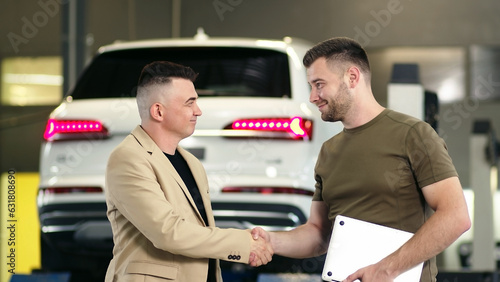 service station, a young professional man shows a satisfied client on a tablet the technical condition of the car, smiles and gives the keys to the car