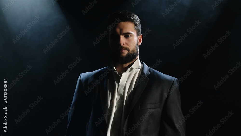 Fototapeta premium Portrait of a bearded man sitting with a serious face, against a dark background.