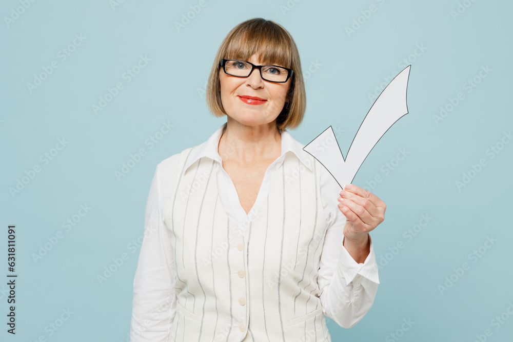 Blonde successful employee business woman 50s wear white classic suit glasses formal clothes hold in hand check mark look camera isolated on plain pastel blue background. Achievement career concept. Blonde successful employee business woman 50s wear white classic suit glasses formal clothes hold in hand check mark look camera isolated on plain pastel blue background. Achievement career concept.