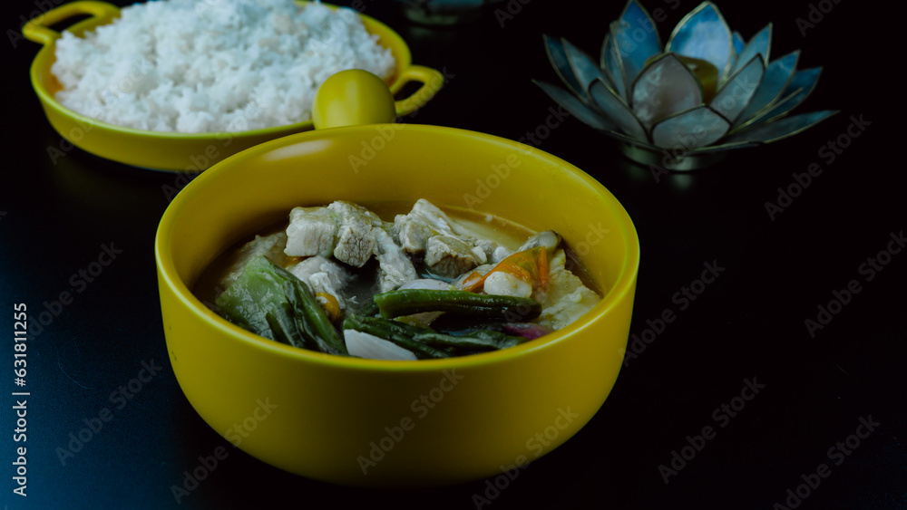 Filipino Sinigang served together with steamed rice in yellow bowls over black table sheet. candle decoration. overhead view