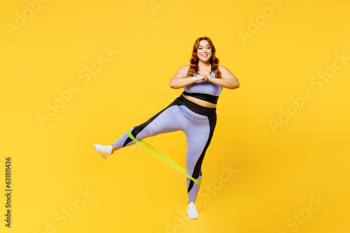 Full body young chubby plus size big fat fit woman wear blue top warm up train use rubber elastic bands for legs look camera isolated on plain yellow background studio home gym. Workout sport concept.