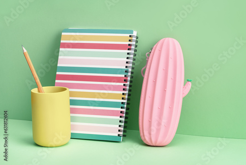 One spiralbound notepad with pink cactus pencil case on green. Back to School or drawing and creativity concept. Copy space. Mockup banner photo
