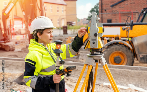 Female site engineer surveyor working with theodolite total station EDM equipment on a building construction site outdoors