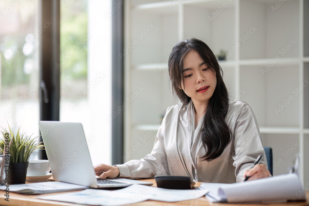 Asian Business woman using laptop for doing math finance on an office desk, tax, report, accounting, statistics, and analytical research concept Asian Business woman using laptop for doing math finance on an office desk, tax, report, accounting, statistics, and analytical research concept