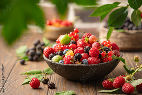 Various fresh berries in a bowl. Mix of different fresh berries on wooden background. Strawberries, raspberries, gooseberries and cherries are presented.