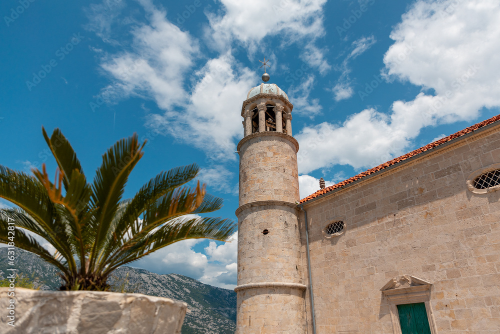 Summer vacation. View of old historical building with tower and palm tree against background of blue sky and clouds. Travel and tourism in Montenegro