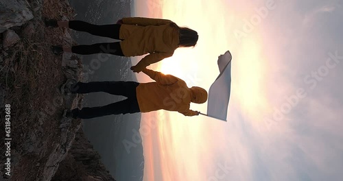 Vertical shot man waving white flag holding a woman's hand against sunset dawn. Couple standing on the top of the mountain with white flag in man's hand. Concept of peace and freedom photo