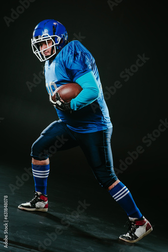 Portrait of a man in a blue uniform for american football runs with a ball on a black background. 